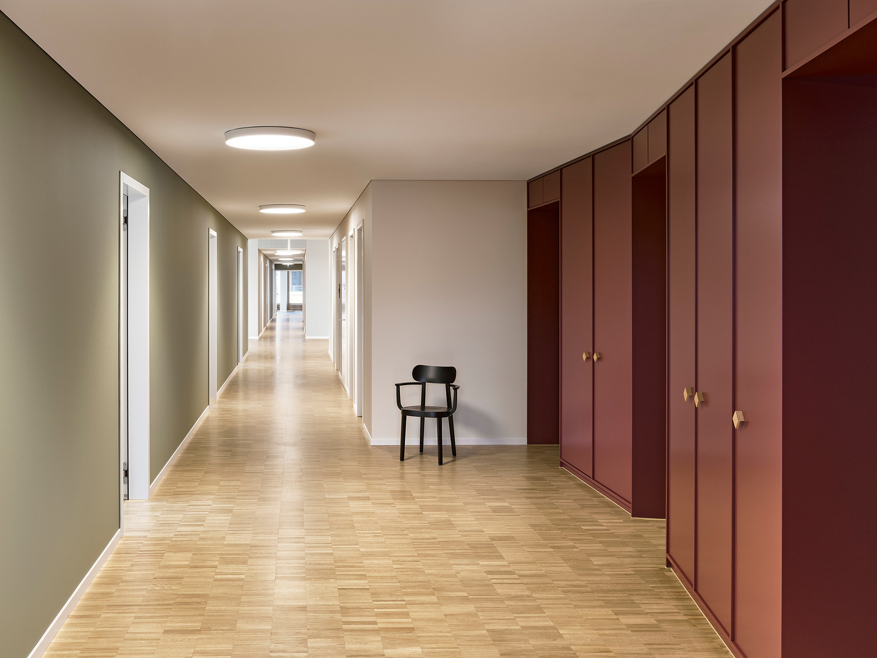 Harmonisch gestalteter Korridorbereich in der Praxis mit Parkettboden und weinroten Schreinerarbeiten.