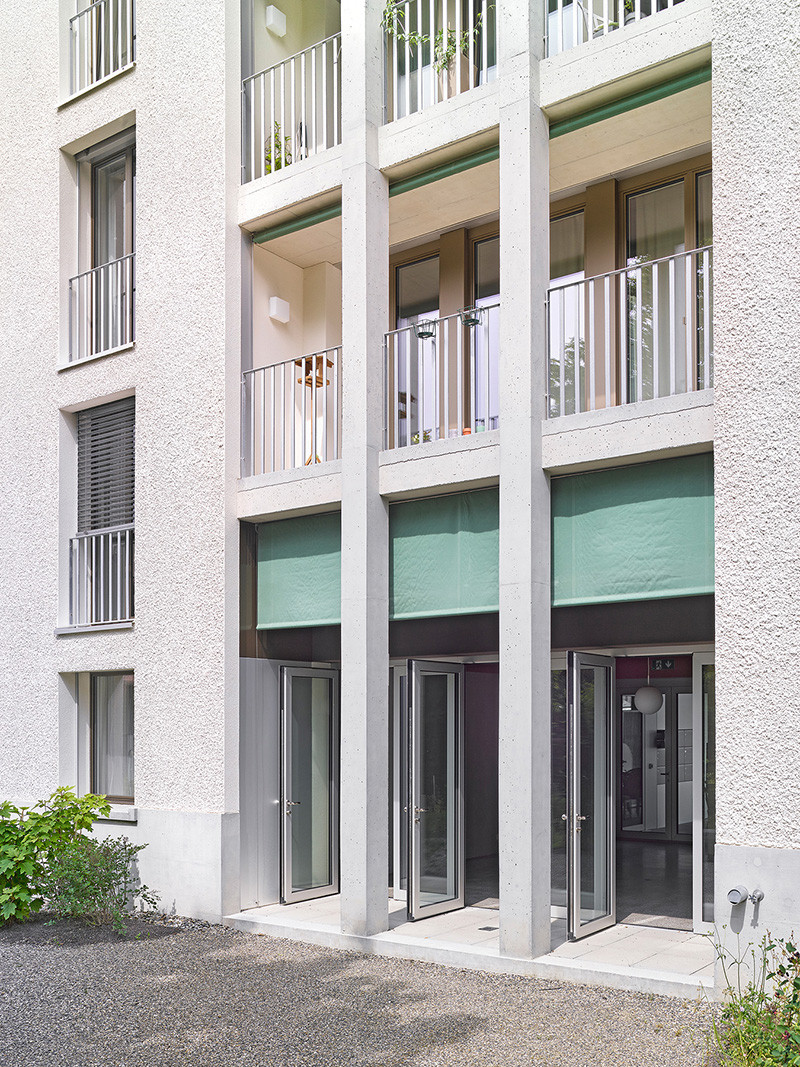 Erdgeschossfassade an der Westseite mit Arkaden, überhohem Gemeinschaftsraum und Gartenzugang.