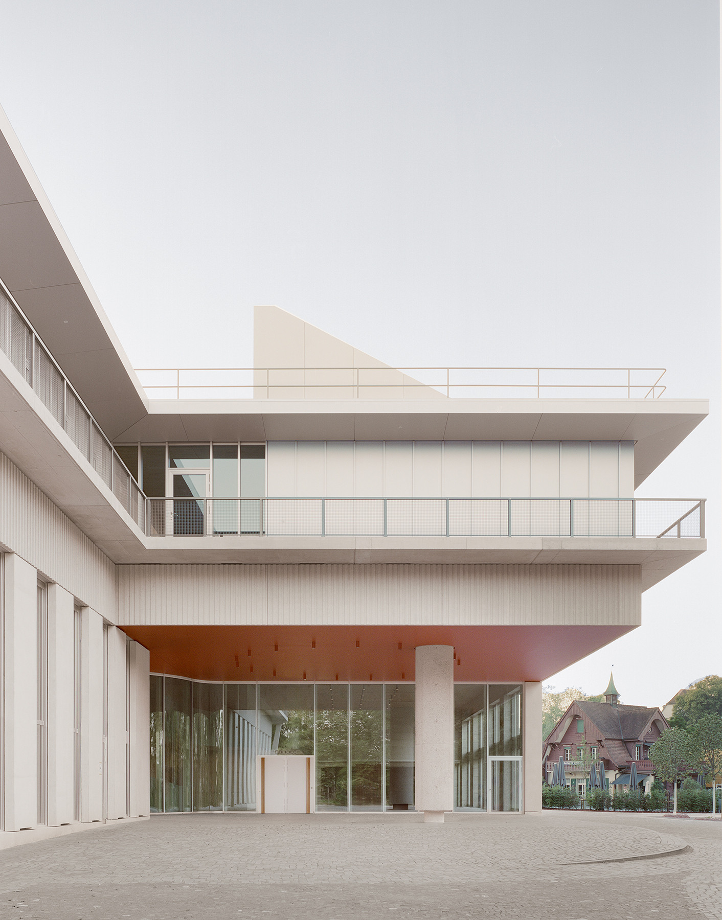 Perspektive auf den Haupteingang des Schulhaus Zirkusplatz mit gedecktem Vorbereich und Fassadenstruktur.